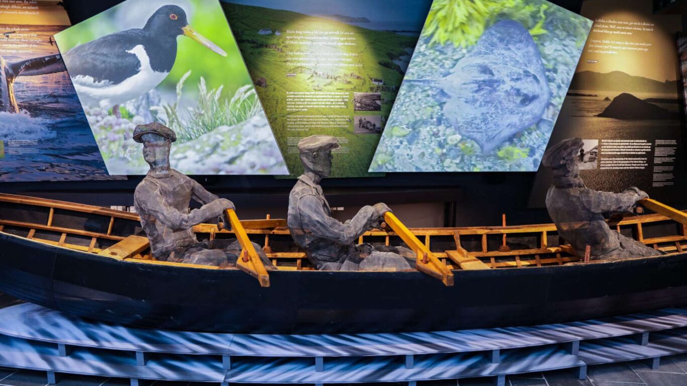 Exhibit of three wooden fisherman mannequins rowing a boat, with informational wildlife panels displayed in the background.