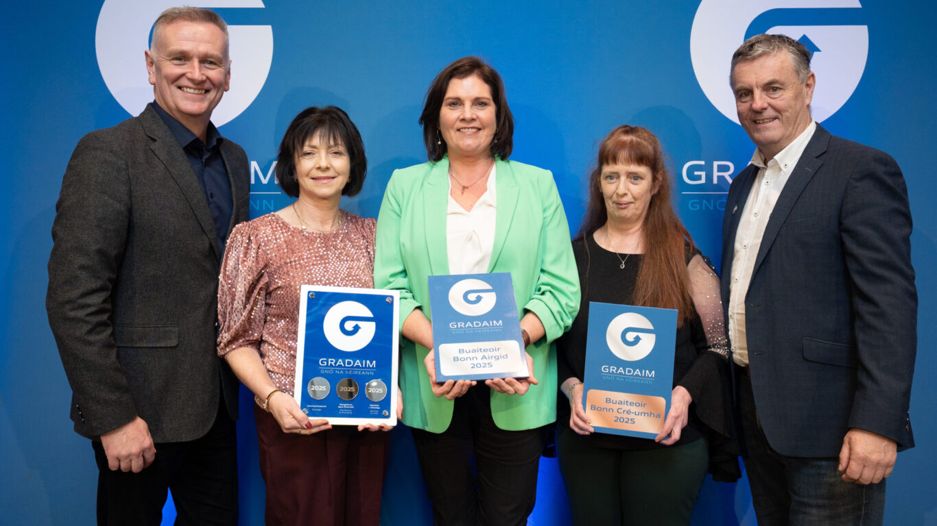 Five people stand in front of a blue backdrop with the Gradam logo, two holding plaques labeled