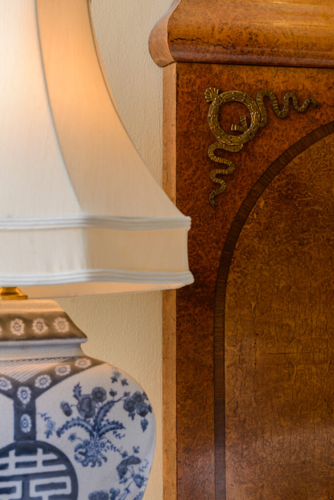 A ceramic lamp with a floral and geometric pattern stands next to a wooden headboard with a decorative metal snake detail.