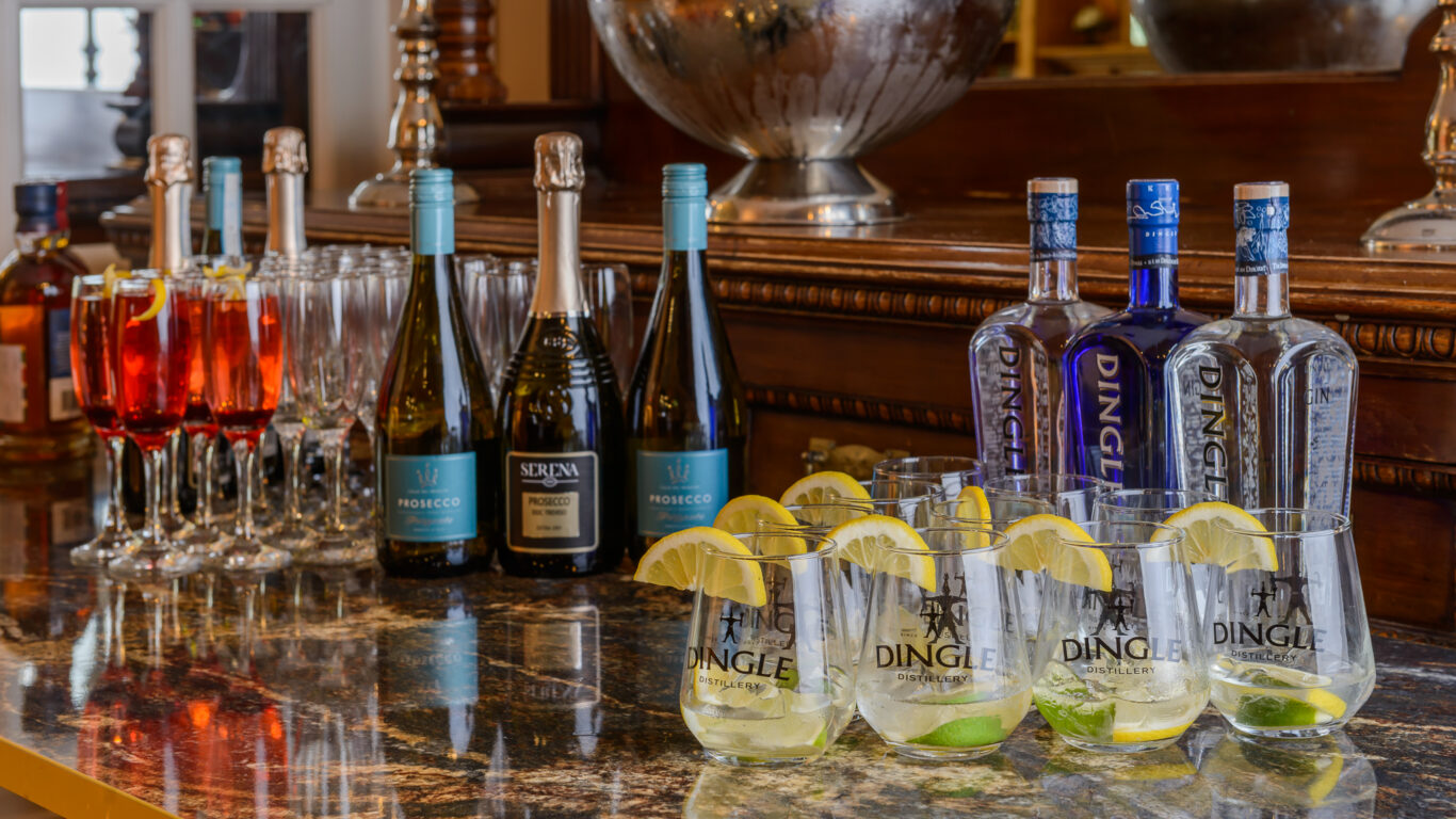 Bottles of prosecco, gin, and cocktail glasses with lemon and lime slices arranged on a marble countertop with glassware.