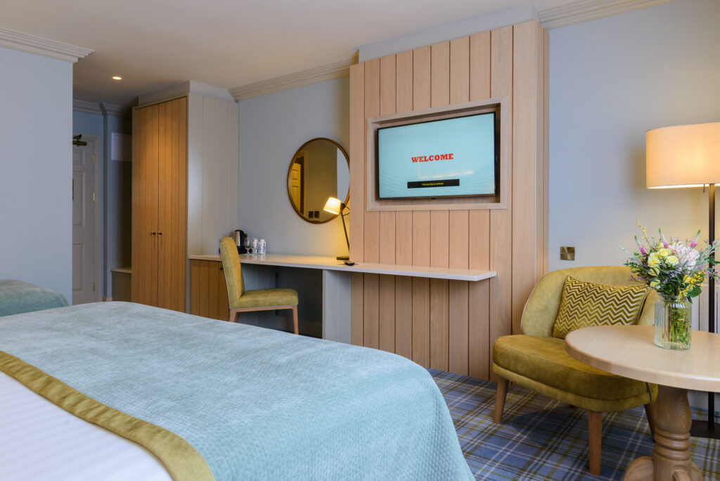 A modern hotel room with a bed, a desk and chair, a wall-mounted TV displaying 